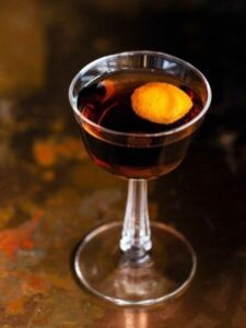 Dunkler Aperitif mit Orangenzeste in einem eleganten Stielglas