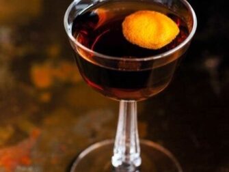 Dunkler Aperitif mit Orangenzeste in einem eleganten Stielglas